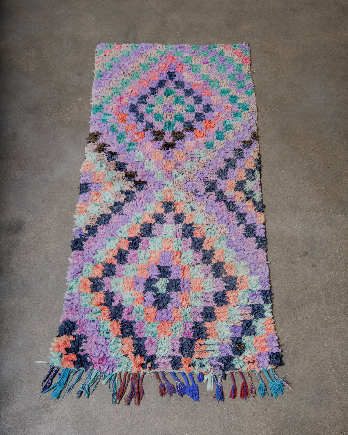 lavender woven rug with a geometric pattern on a concrete floor.